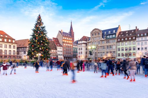 People ice skating in the middle of the town centre with a big Christmas tree in the background