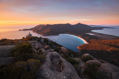 Lookout to  a crescent-shaped beach surrounded by lush green forested hills at sunset 