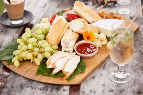A close-up photo of a wooden board full of produce like grapes, cheeses, crackers and dips. 