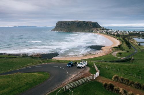 Two cars parked at the side of the road for a lookout at The Nut which is a giant volcanic flat-topped mountain at the edge of a coastal village