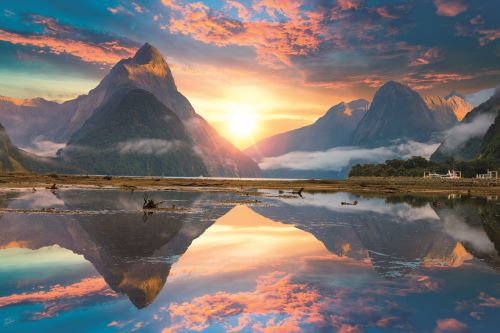 Sun setting behind majestic mountains colouring the sky in shades of pink and purple and reflecting in the still water