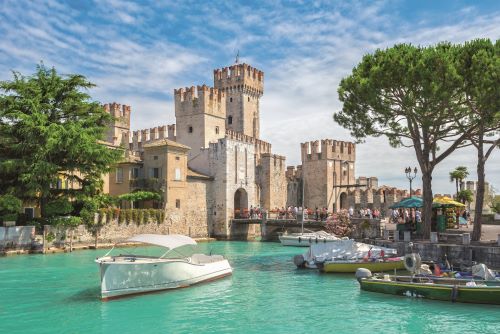 Some boats parked in a canal next to a big castle.