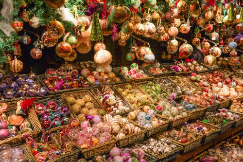 Colourful Christmas baubles and ornaments arranged in wicker baskets and hanging from the ceiling at a European Christmas market stall.