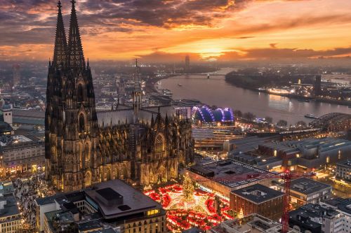 Cologne Cathedral and Christmas market lights along the Rhine at sunset.
