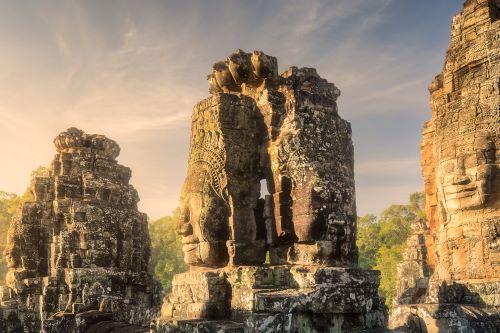 Ancient stone faces carved into the Bayon temple towers in Cambodia, illuminated by the soft golden light of sunset.