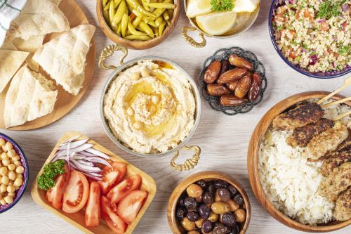 A table filled with Middle Eastern dishes including hummus, pita, salads, olives, rice with grilled meat, and assorted vegetables