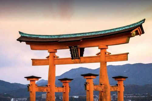 One of Japan's iconic Shinto Torii gates shining in bright orange in front of a dark blue mountainside in the back