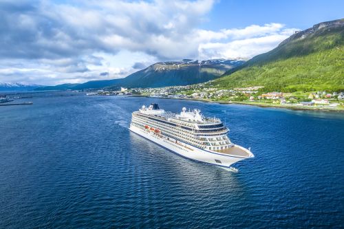 Cruise ship sailing through a calm fjord with green hills and snow-capped mountains in the background