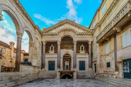 Historic stone courtyard with arched columns and ornate architecture under a bright blue sky