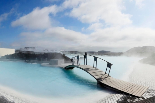 A thermal pool with turquoise evaporating water and a small wooden bridge
