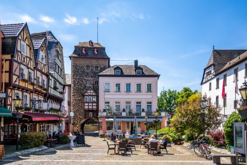 Small buildings in a European town with tables and chairs and tourists sitting down enjoying the sunshine