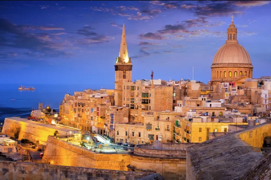 View of Valletta with its honey-coloured limestone building set against the Mediterranean Sea at dusk.