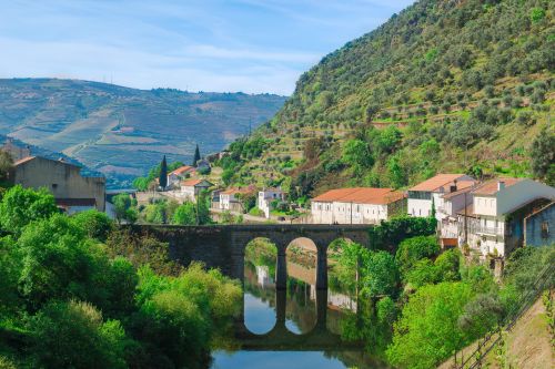 Tall mountains leading down to a river with houses and a bridge
