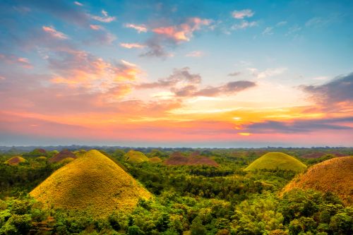 The Chocolate Hills of Bohol rising above lush green forest at sunset
