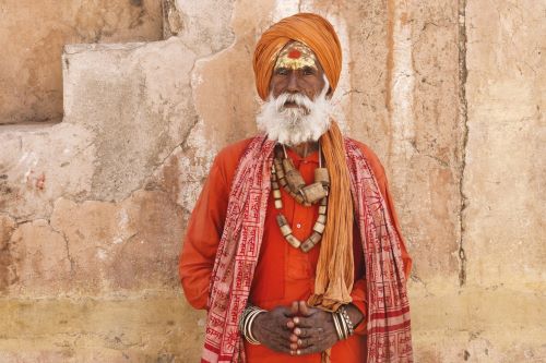 Indian man wearing a bright orange traditional clothing and headdress looking straight into the camera. 