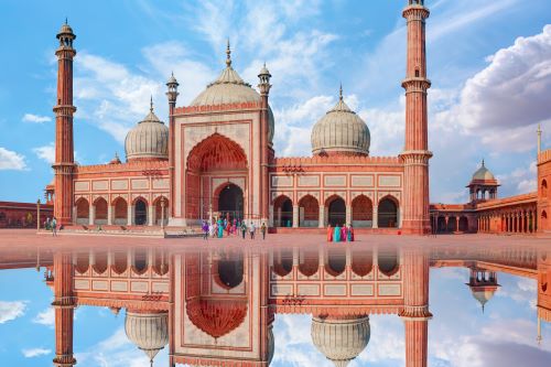 A grand, centuries-old mosque with towering minarets and a large courtyard reflecting in the water