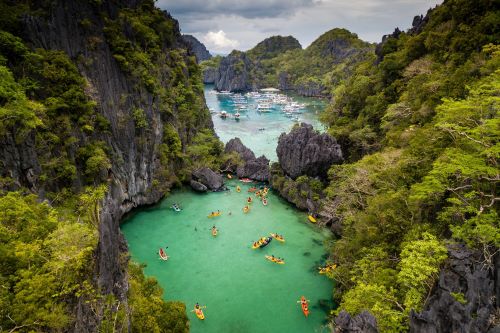 Some kayaks paddling in crystal-clear turquoise waters surrounded by lush green forests covering stunning limestone cliffs towering from the water.