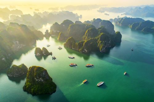 Aerial view of Ha Long Bay with emerald waters dotted with boats, towering limestone islands and lush greenery.