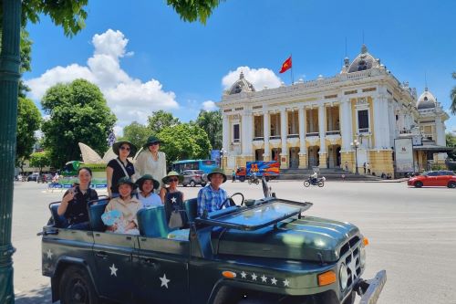 Tourists in a vintage jeep posing in front of the Hanoi Opera House on a sunny day.