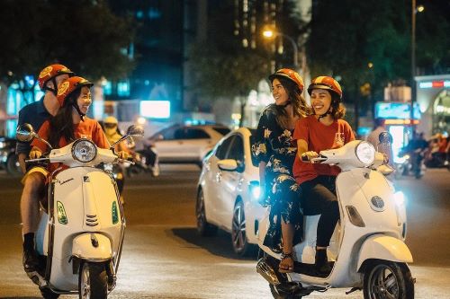 Smiling tourists driving vespas in Ho Chi Minh City by night. 