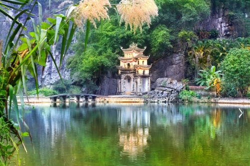 Ancient temple surrounded by lush greenery and reflected in a calm lake in Ninh Binh, Vietnam.