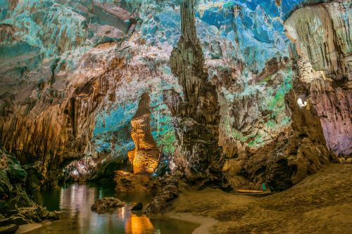 Dramatic limestone formations and an underground river winding through vast, illuminated chambers.