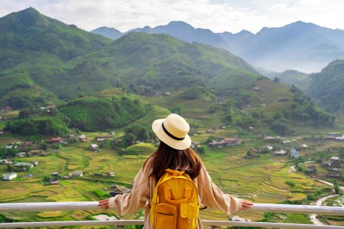 A traveller from the back overlooking scenic mountain town of Sapa with its misty valley and terraced rice fields. 